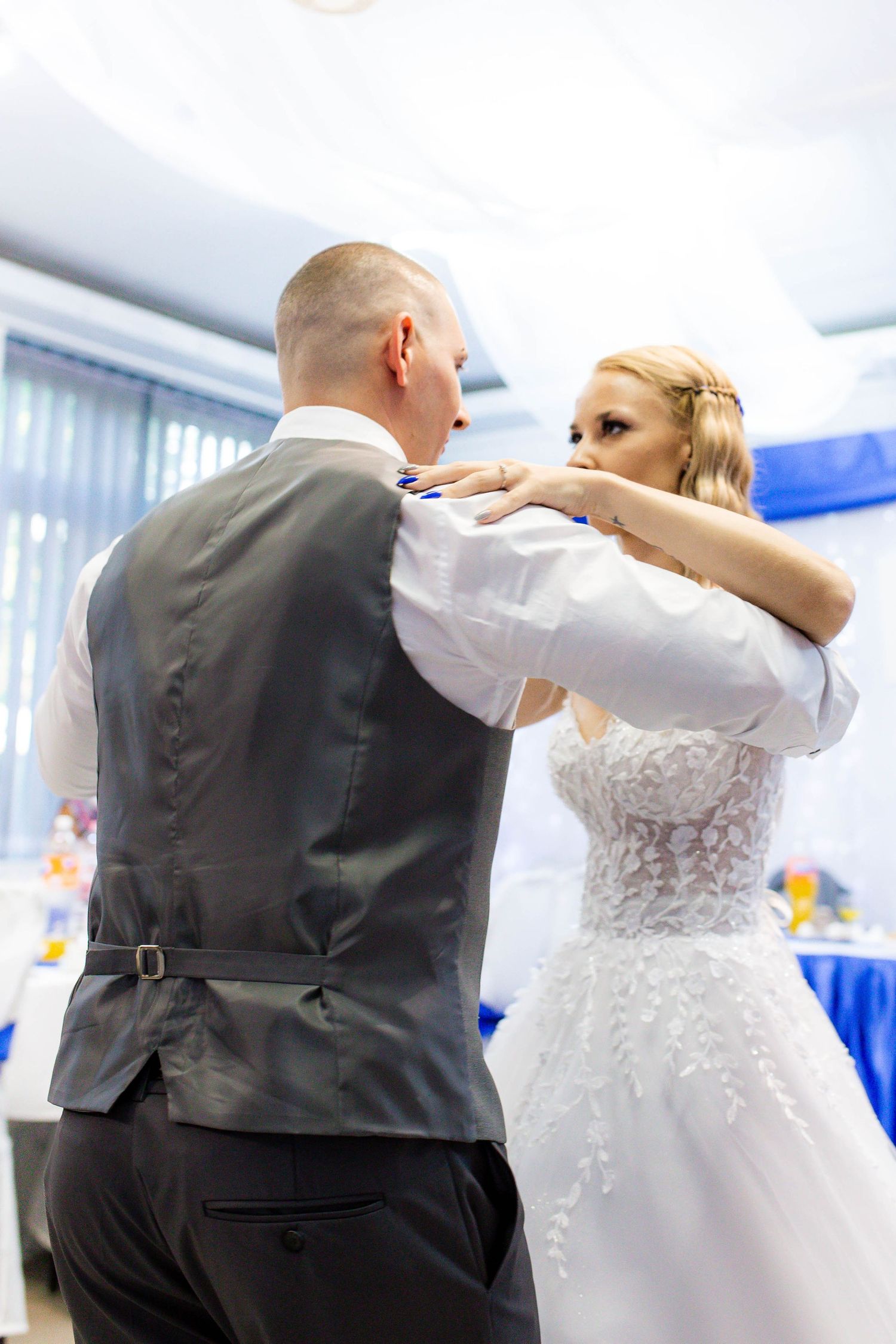 A couple dances together at a wedding reception, with the bride in a white lace dress and groom in a dark vest.