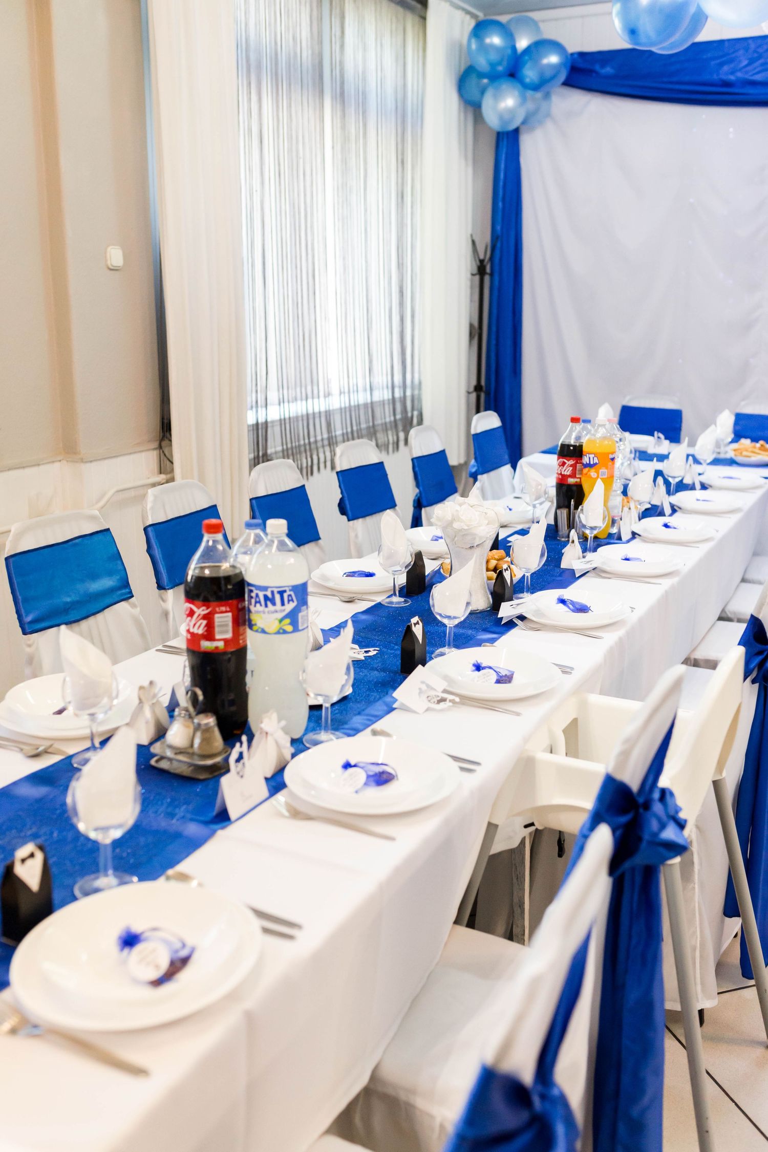 Elegant banquet hall setup with white tablecloths and royal blue decor accents featuring balloon arrangements.