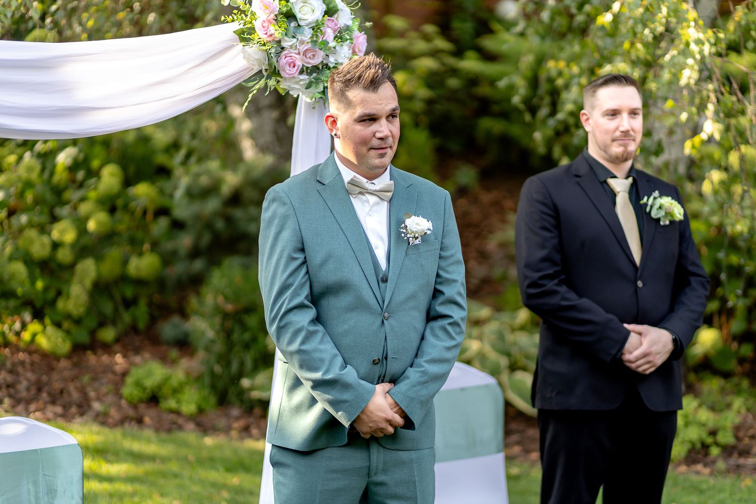 Wedding party members in formal attire stand together outdoors in a garden setting during an autumn celebration.
