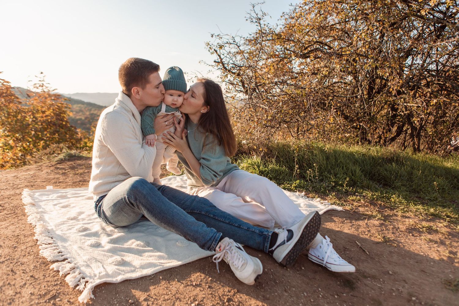 Family relaxing together on white blanket during outdoor autumn photoshoot.