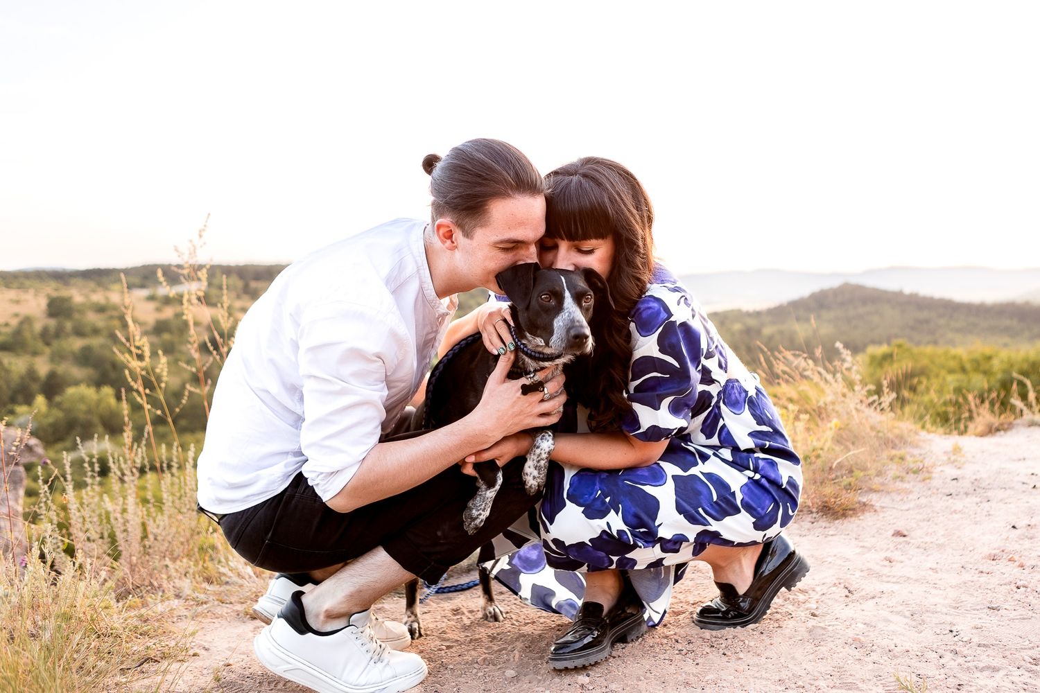 A couple shares a lighthearted moment while sitting on a dirt path at sunset.