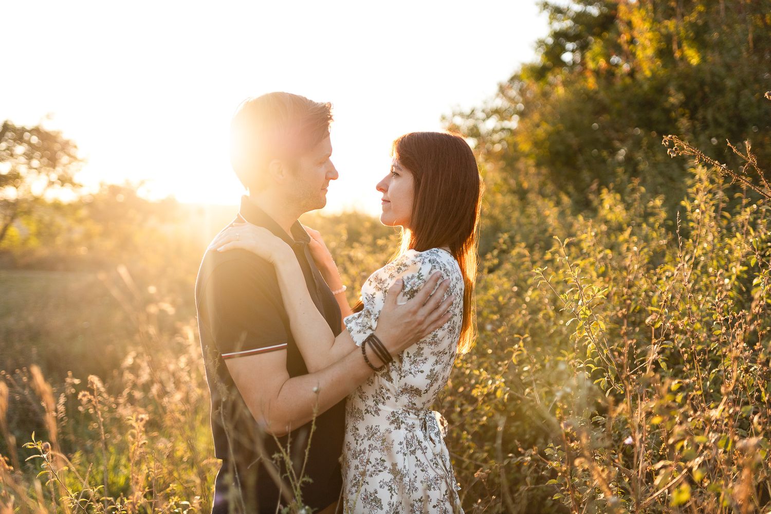 Backlit couple sharing romantic moment in golden sunlit field.