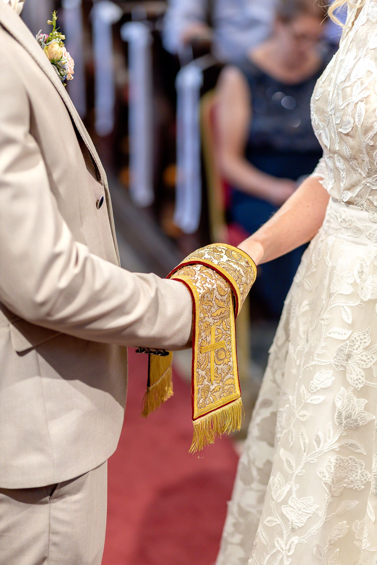 Close-up view of wedding ceremony participants in white and beige attire with gold-trimmed details.