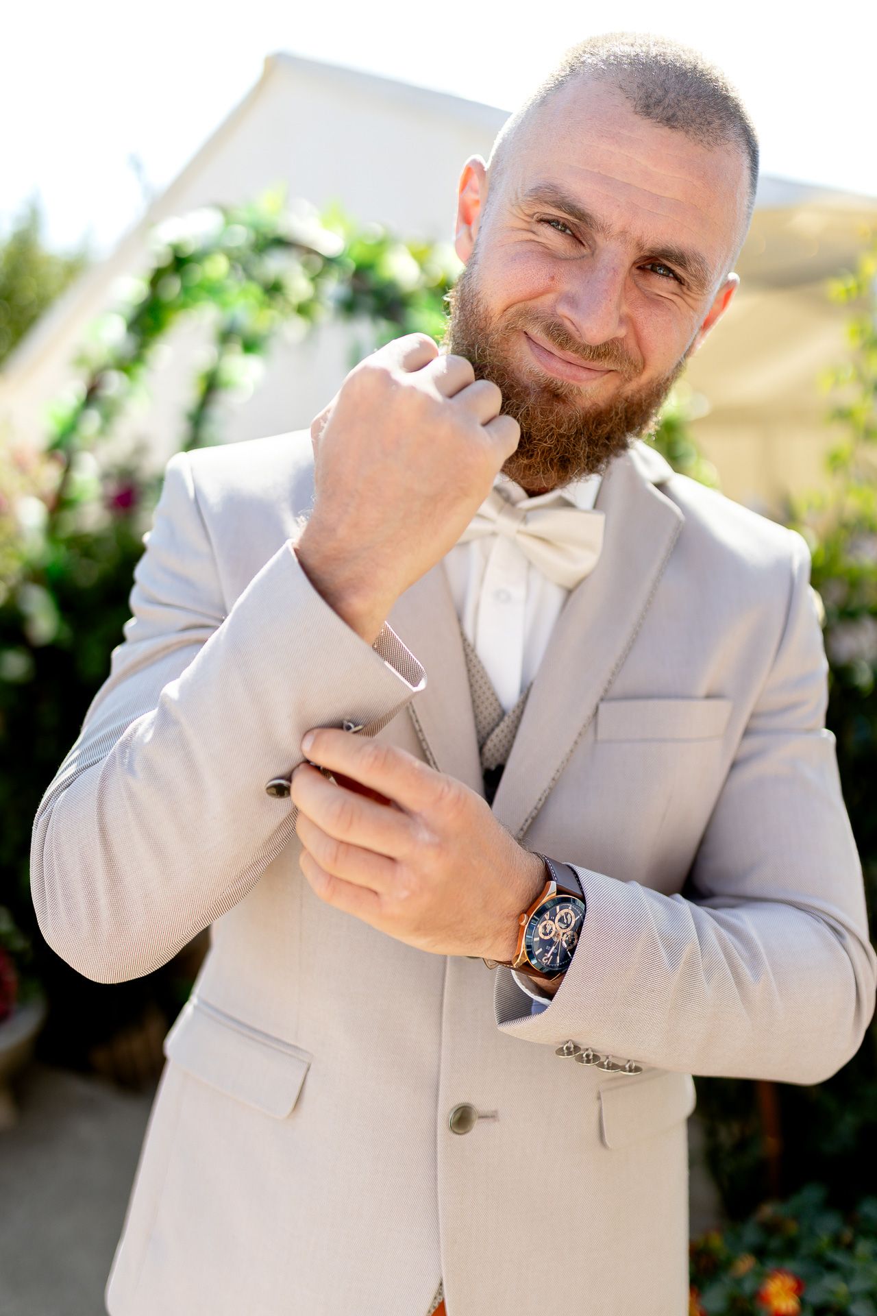 A person in a light gray suit jacket smiles while looking at their phone outdoors.