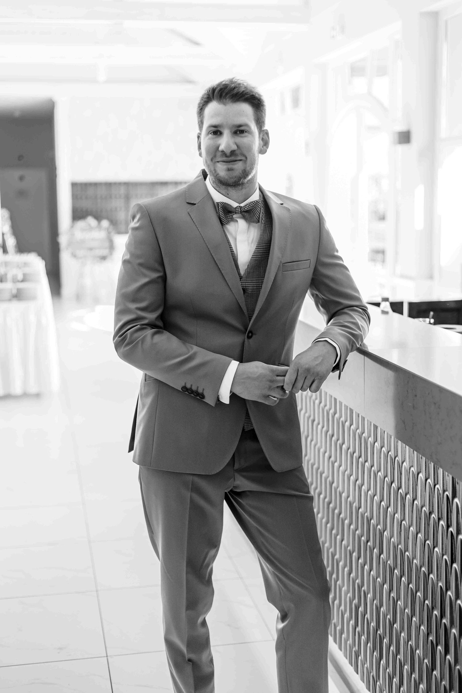 A person in a gray suit stands against a railing in a sequence of four similar poses.