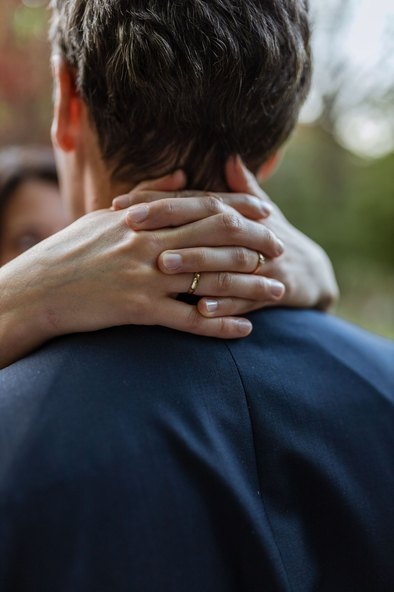 A close-up view shows hands embracing the back of someone wearing a navy blue suit jacket.