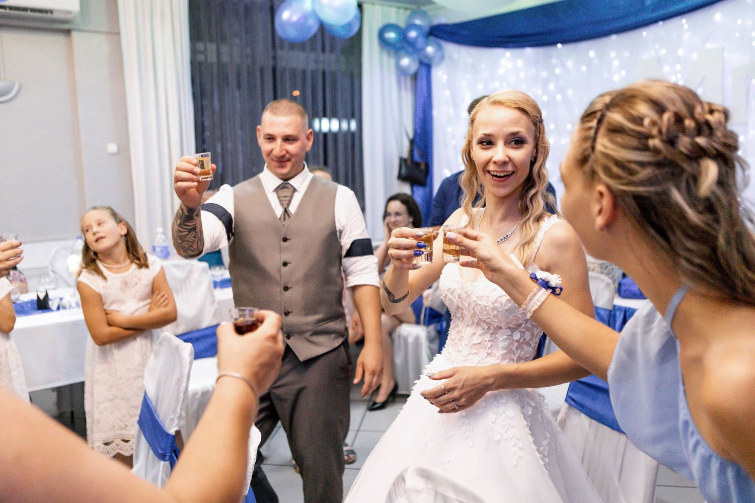 Wedding guests and newlyweds raise their glasses in celebration at a blue and white decorated reception venue.