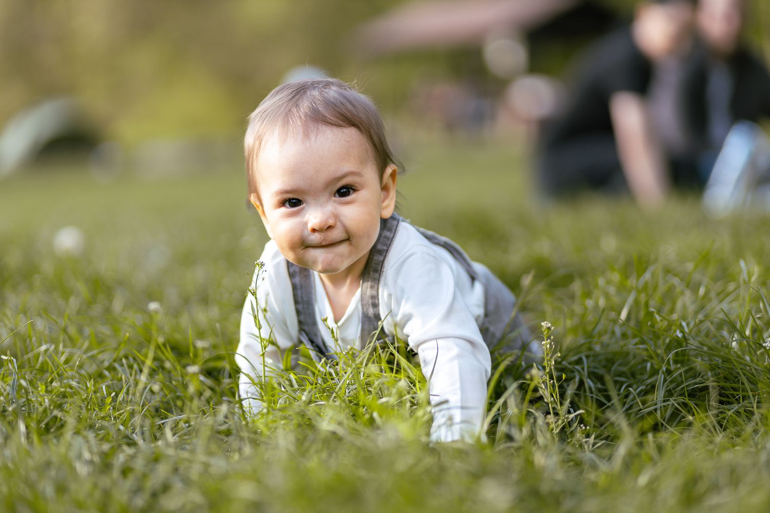 Baby crawling and smiling in green grass during outdoor photoshoot.