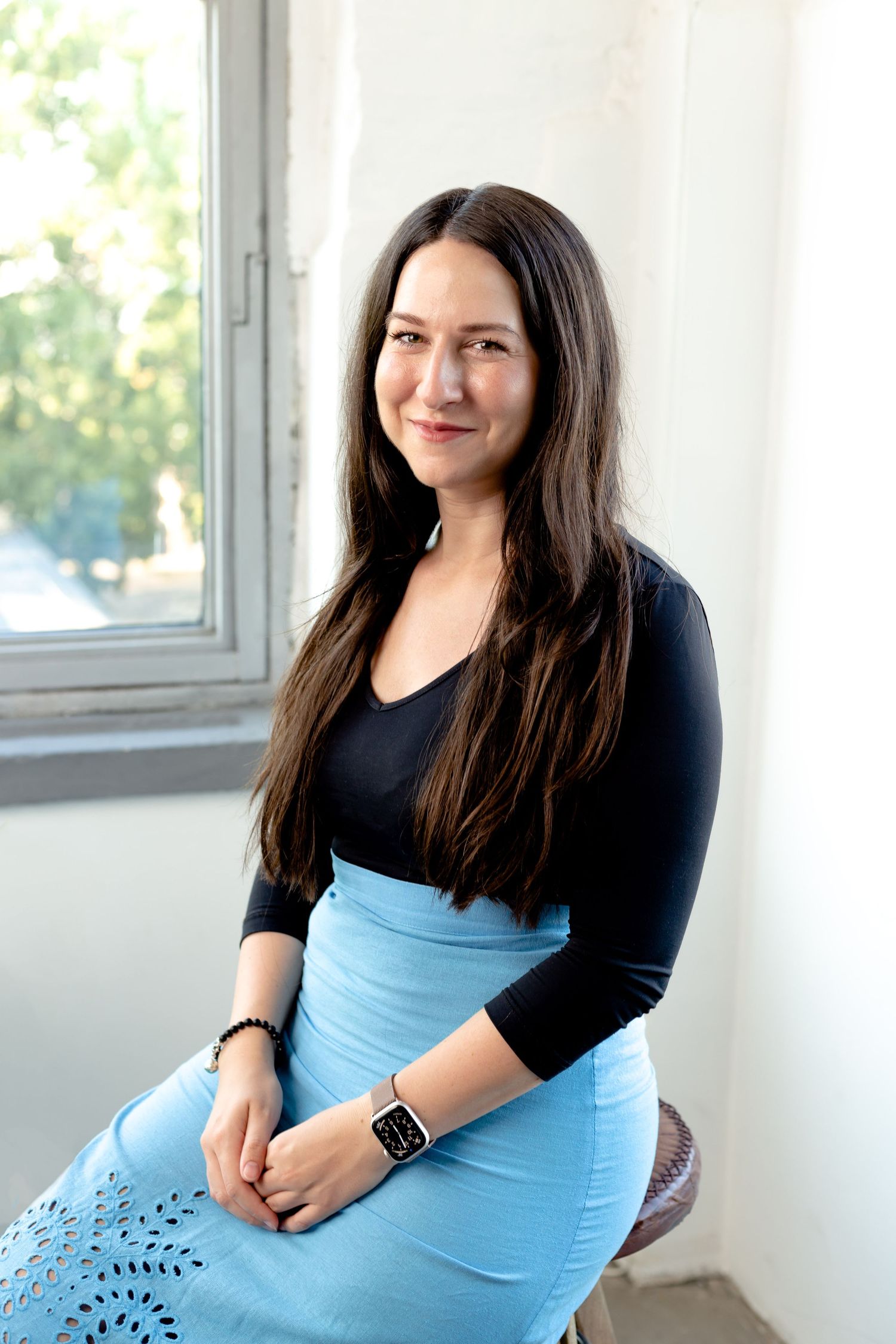 A person in casual attire sits comfortably on a couch in a sunlit room.