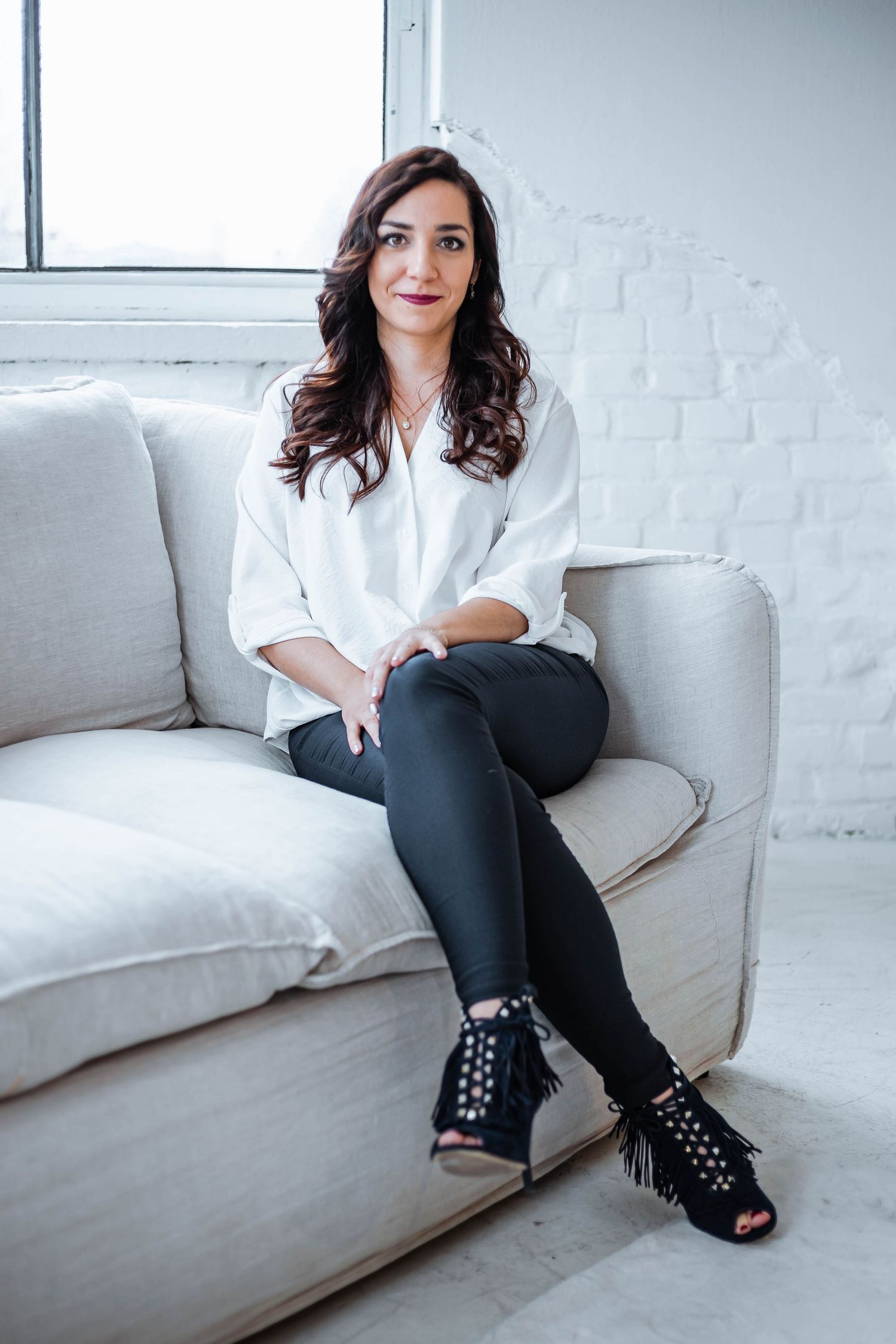 Lifestyle portrait on grey sofa wearing white top and studded black boots.
