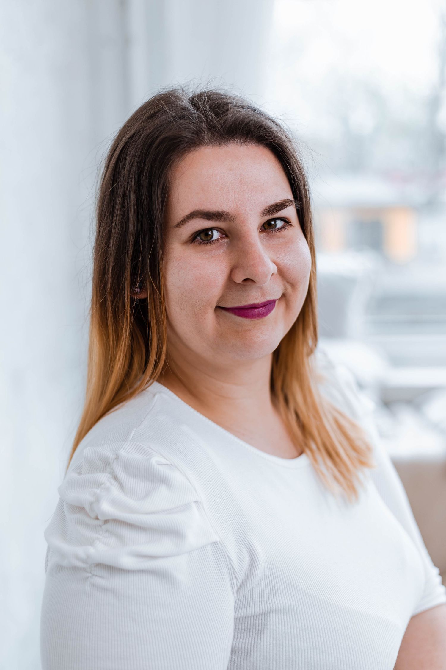Woman with two-toned hair smiles warmly while wearing white top in bright setting.