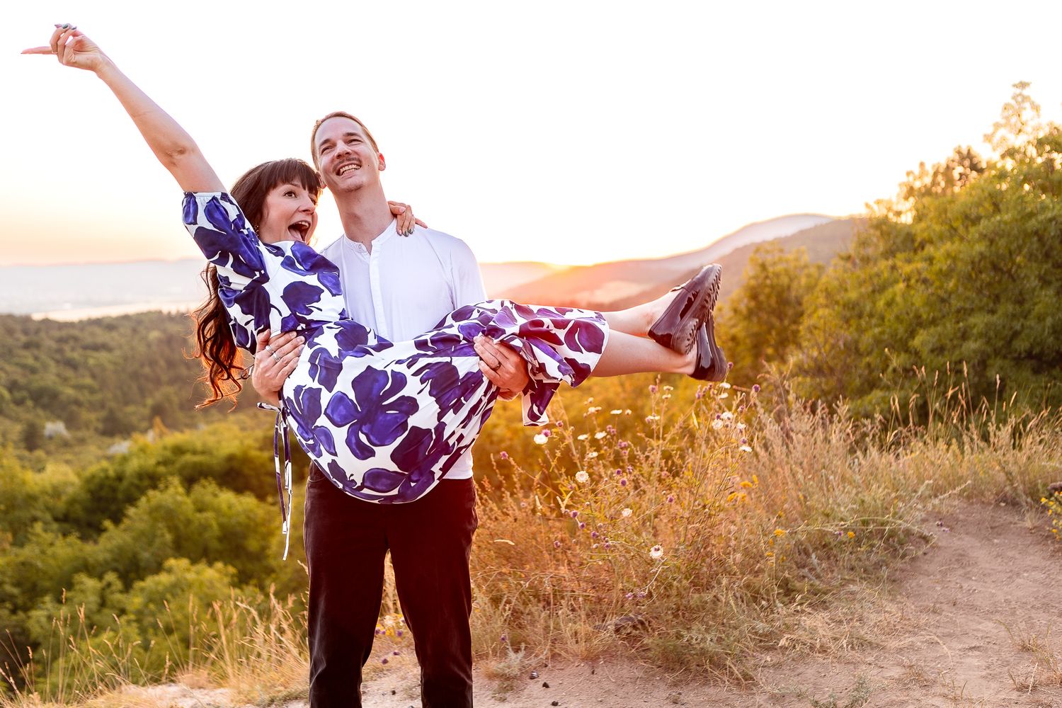 A playful couple poses dramatically on a mountain trail at sunset.