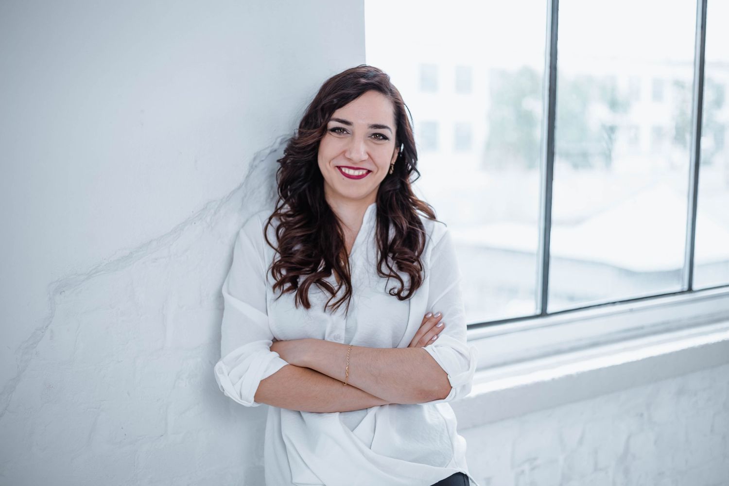 Woman with dark curly hair smiles while sitting in modern bright interior.
