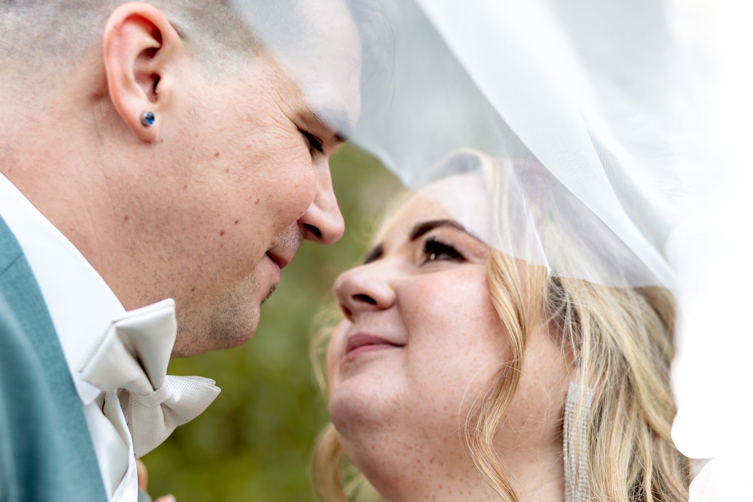 A romantic close-up of a couple in wedding attire sharing an intimate moment outdoors.