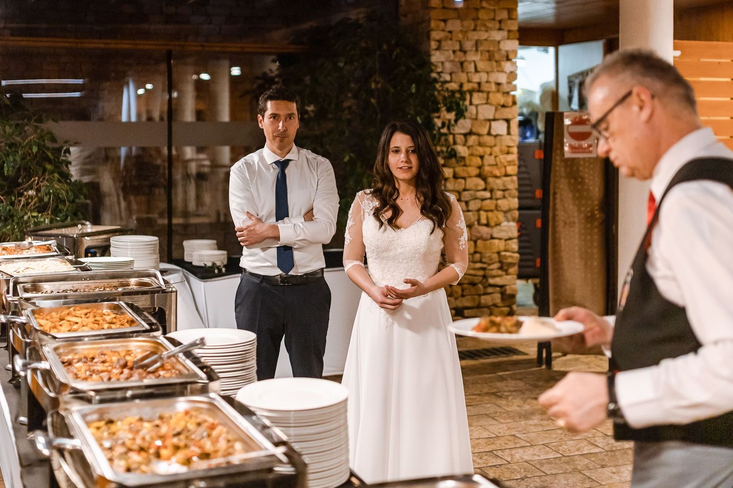 A catering buffet setup at an elegant indoor venue with chafing dishes and servers in formal attire.
