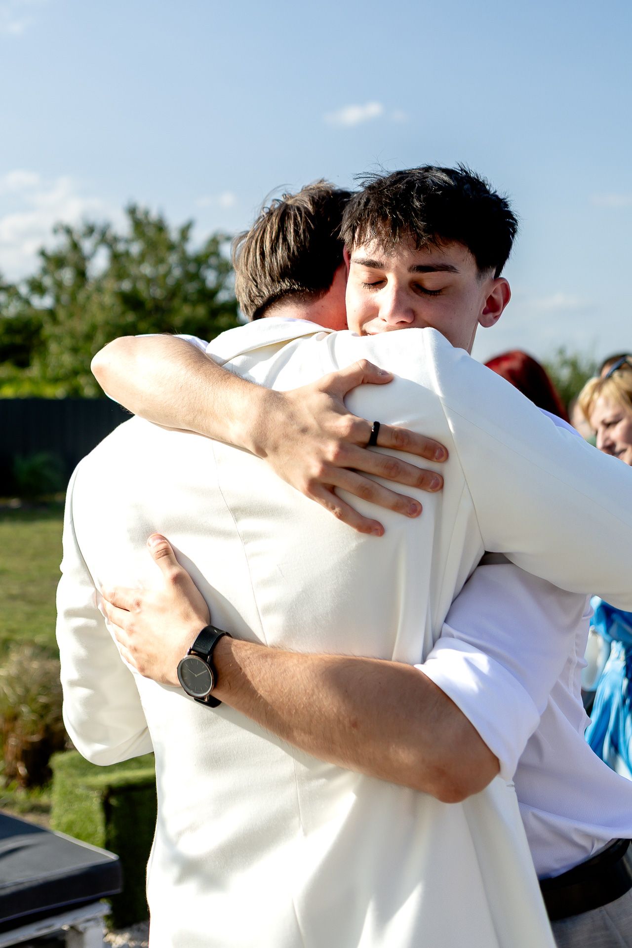 Groomsmen sharing emotional hugs and embraces outdoors.
