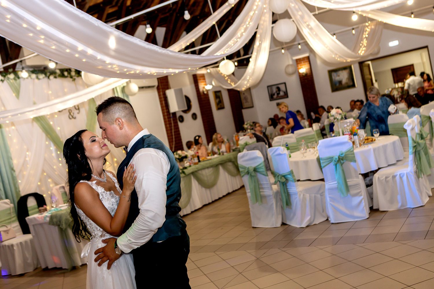 Couples dance together at an elegant wedding reception with white drapes and blue chair covers decorating the venue.