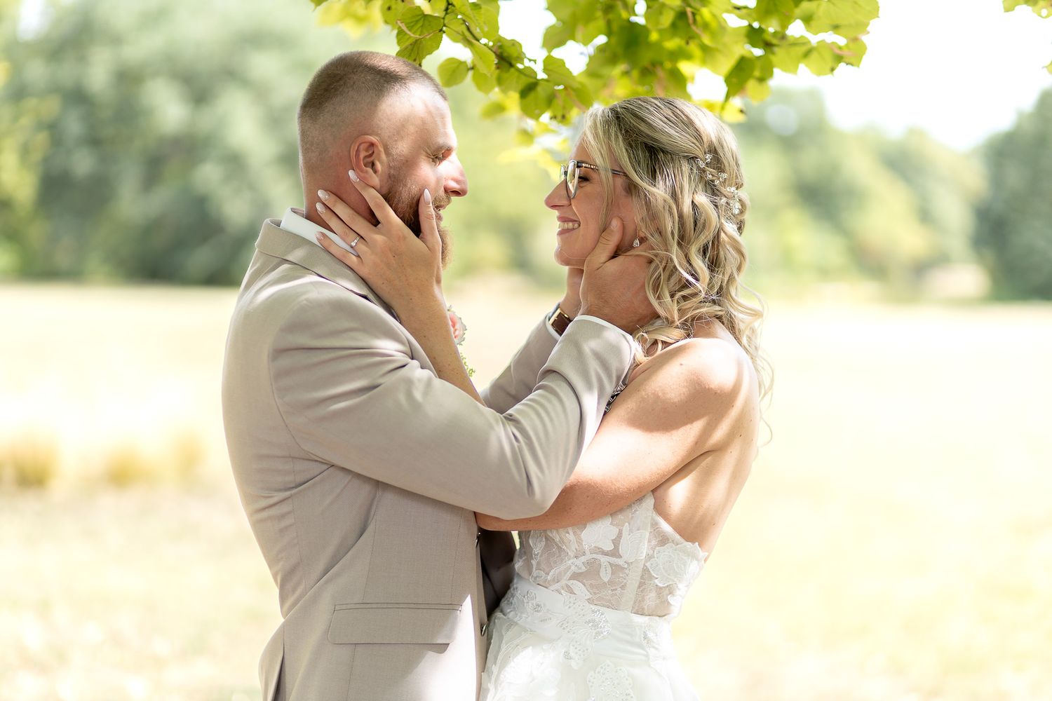 Newlywed couple shares romantic moments in a sunlit meadow wearing white dress and beige suit.