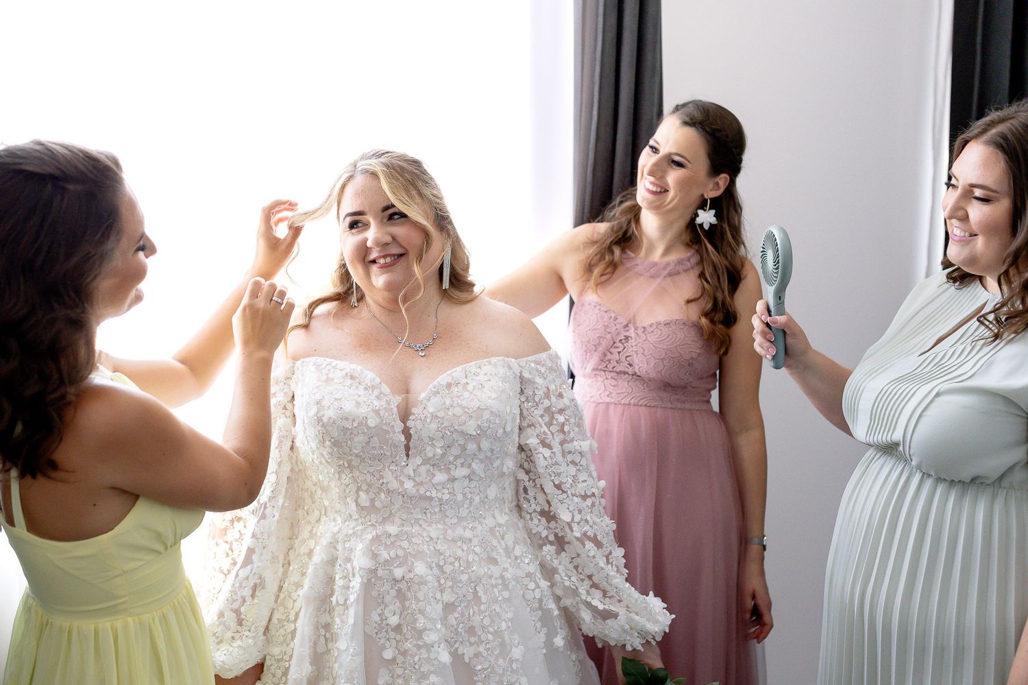 A group of bridesmaids in pastel dresses stand together smiling and laughing during a wedding celebration.