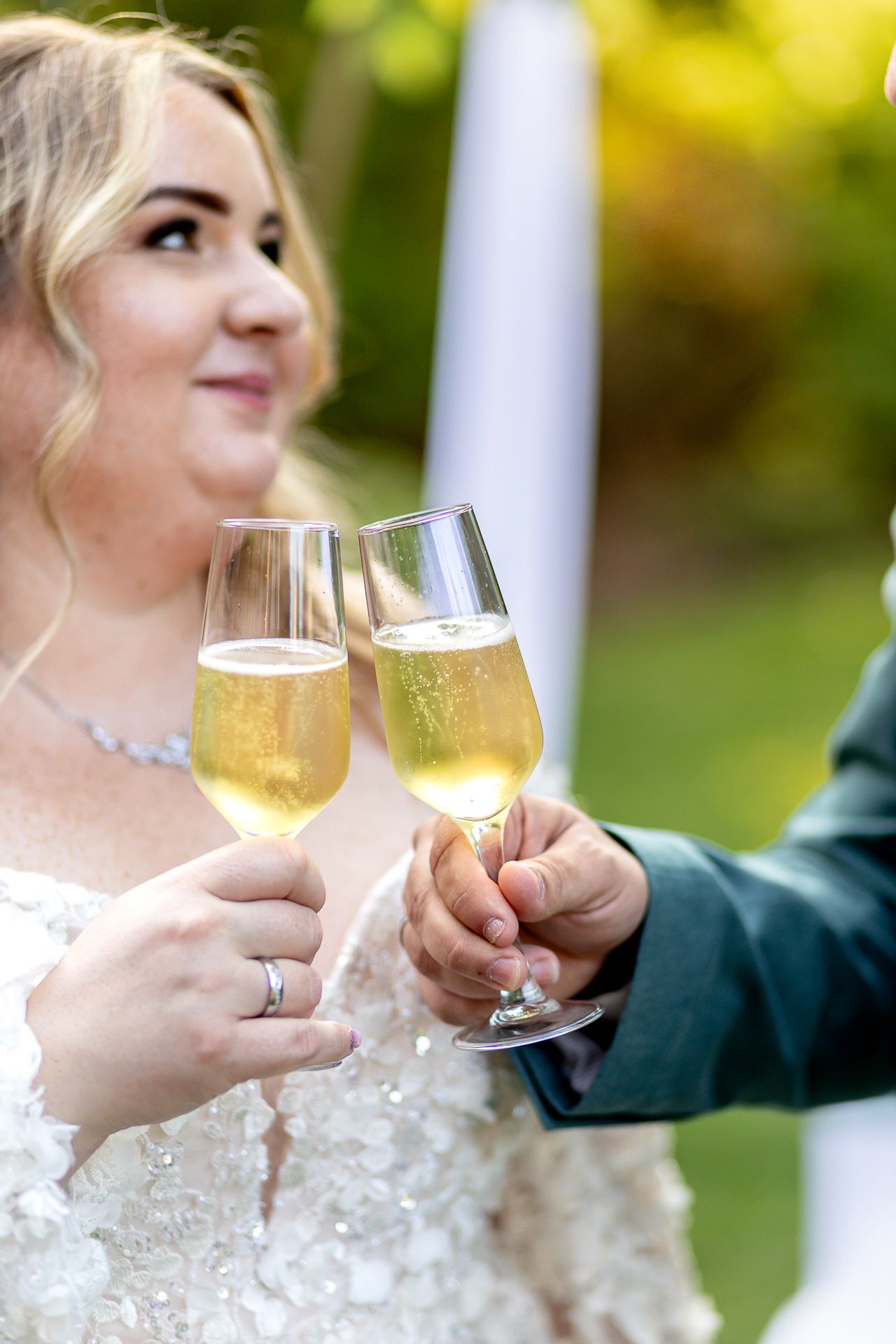 Two champagne glasses clink together in celebration during an outdoor wedding ceremony.
