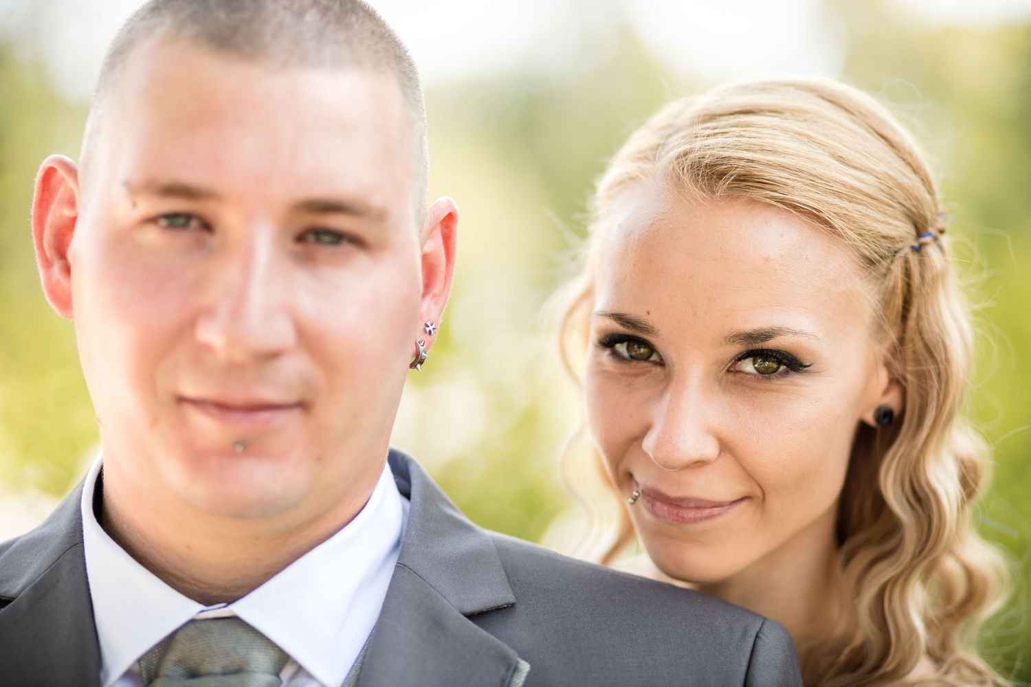 A happy couple poses together outdoors in formal attire with a soft natural background.