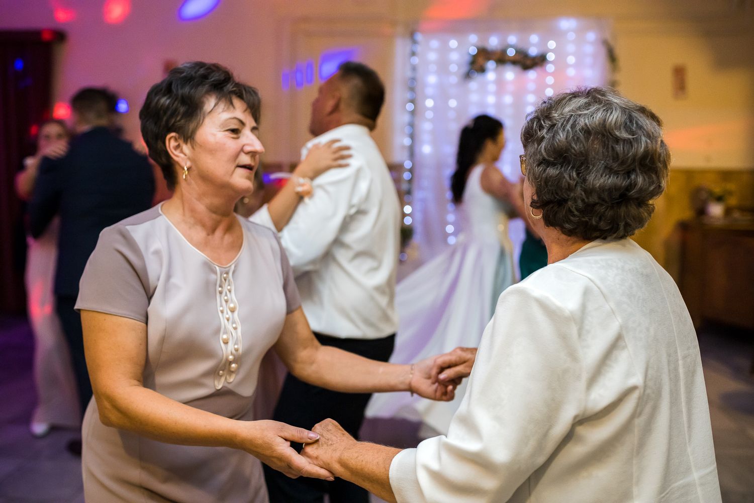 Couples dancing together at an indoor reception venue with colorful lighting and festive atmosphere.
