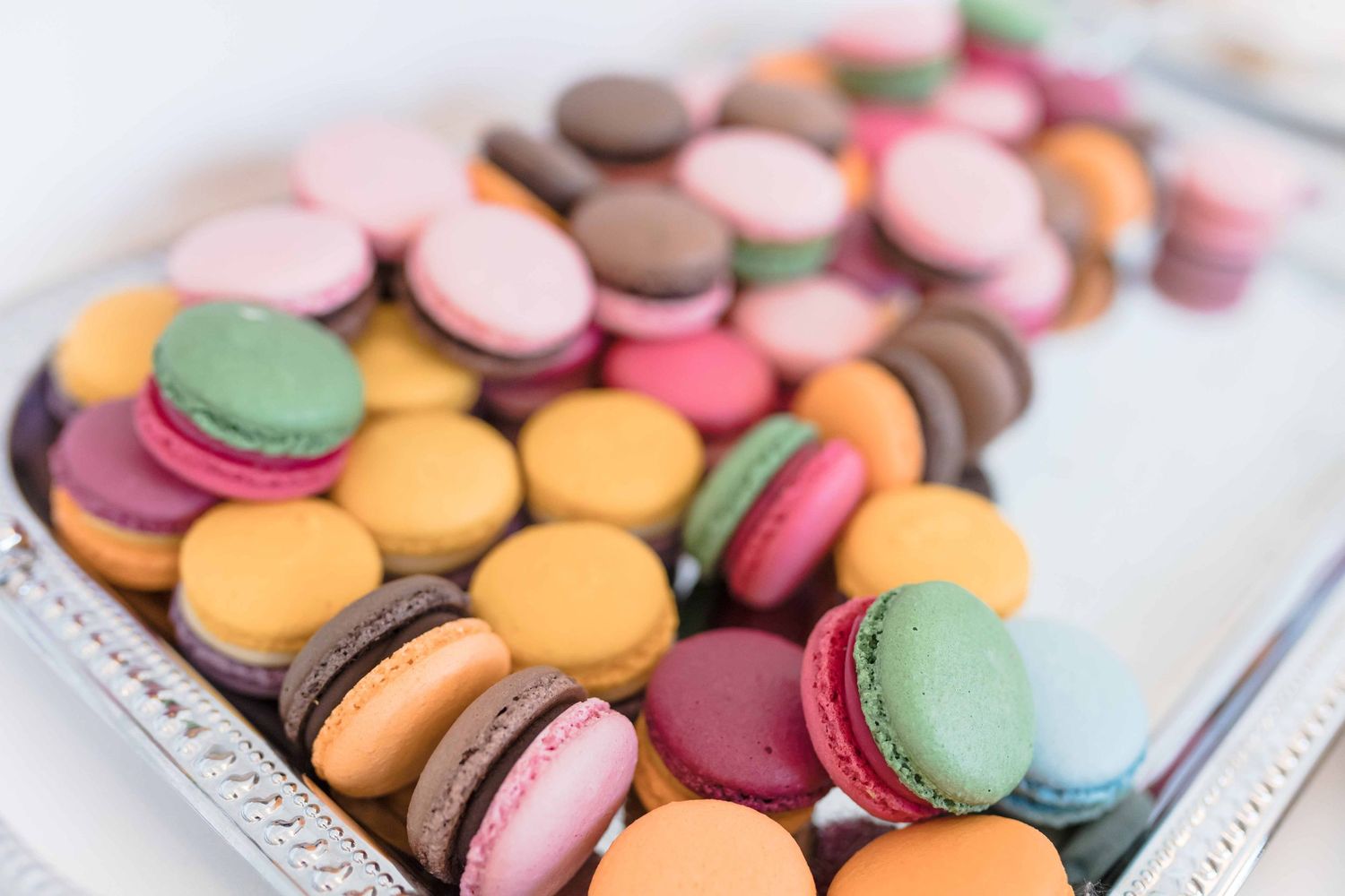 Colorful French macarons in pastel pink, orange, purple and green arranged on white serving plates.