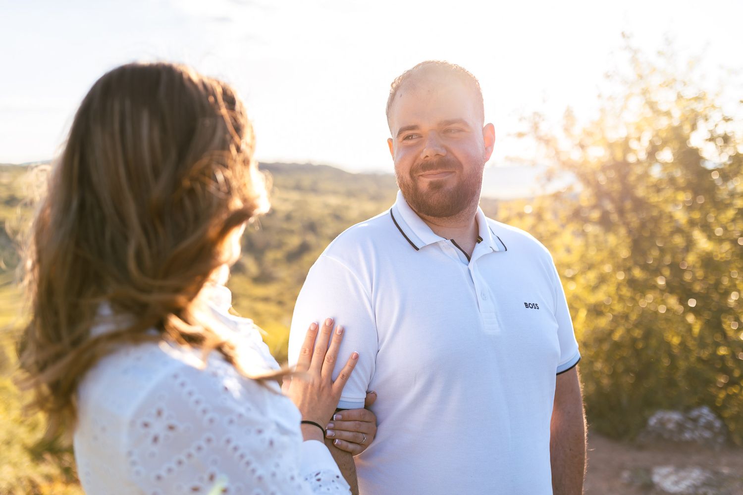 Couple in coordinated white outfits poses against mountain scenery.