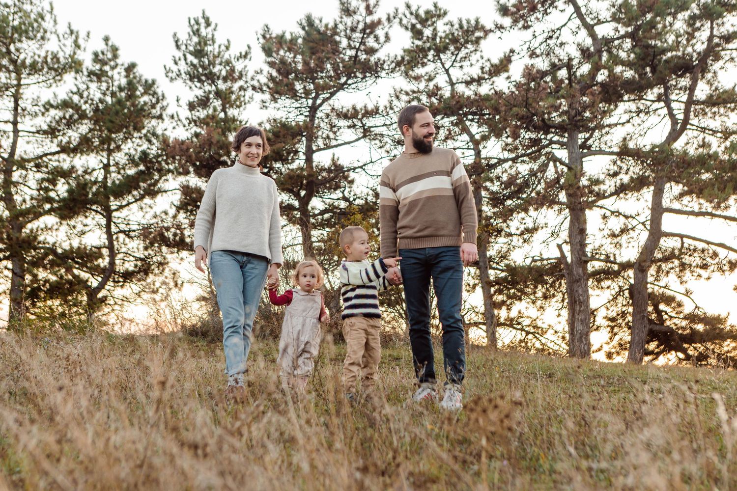 Family walking together on a hilltop path with evergreen trees in the distance.