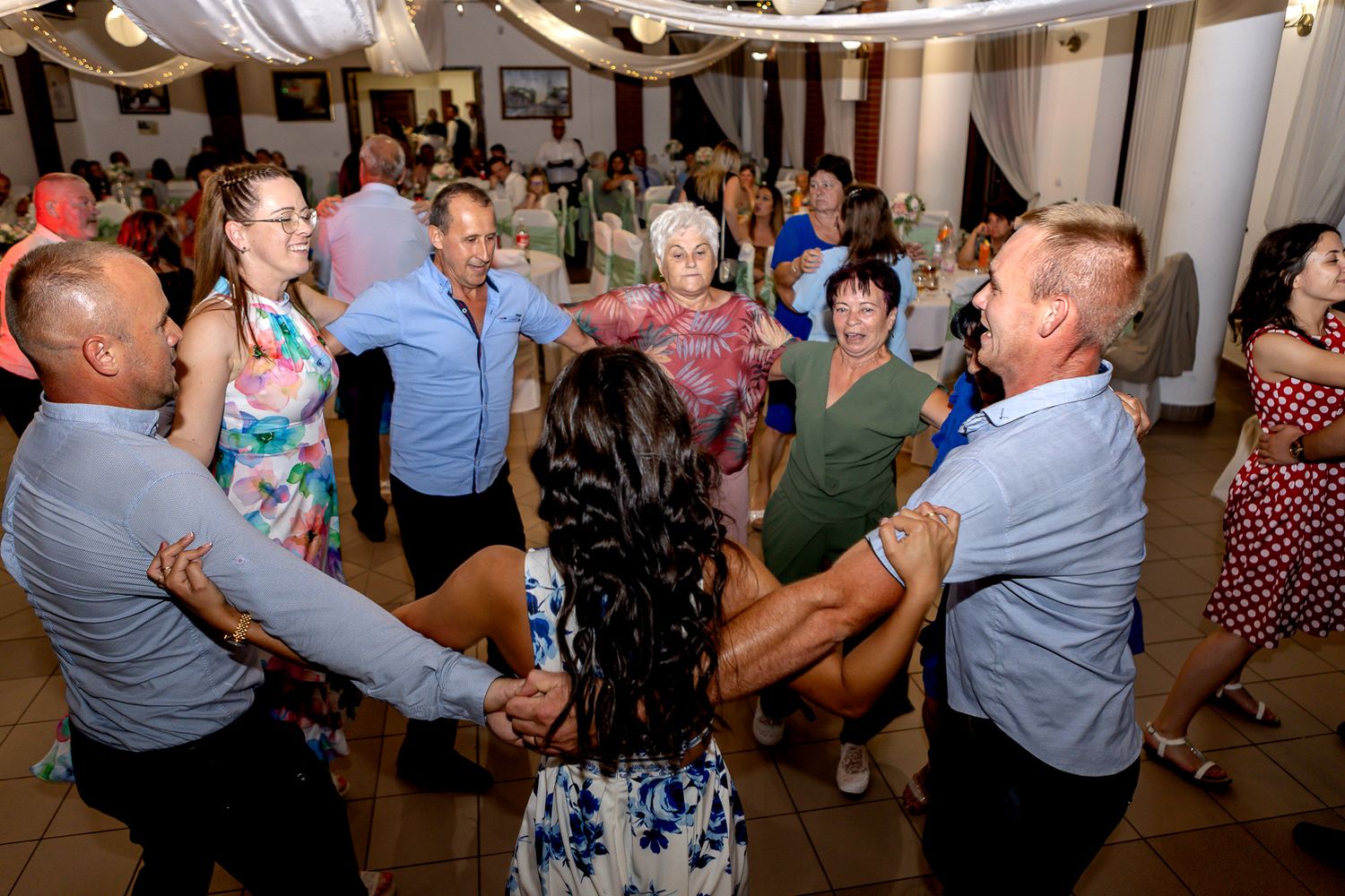 People dancing and celebrating at a lively wedding reception in a decorated indoor venue.