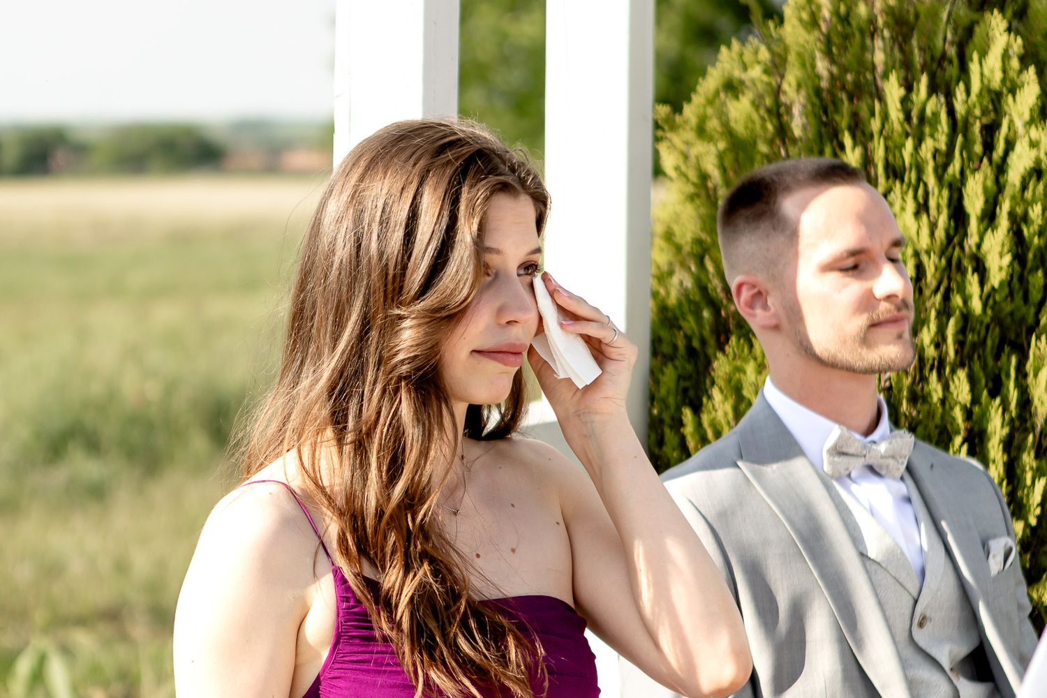 Wedding party members in formal attire stand together during outdoor ceremony.