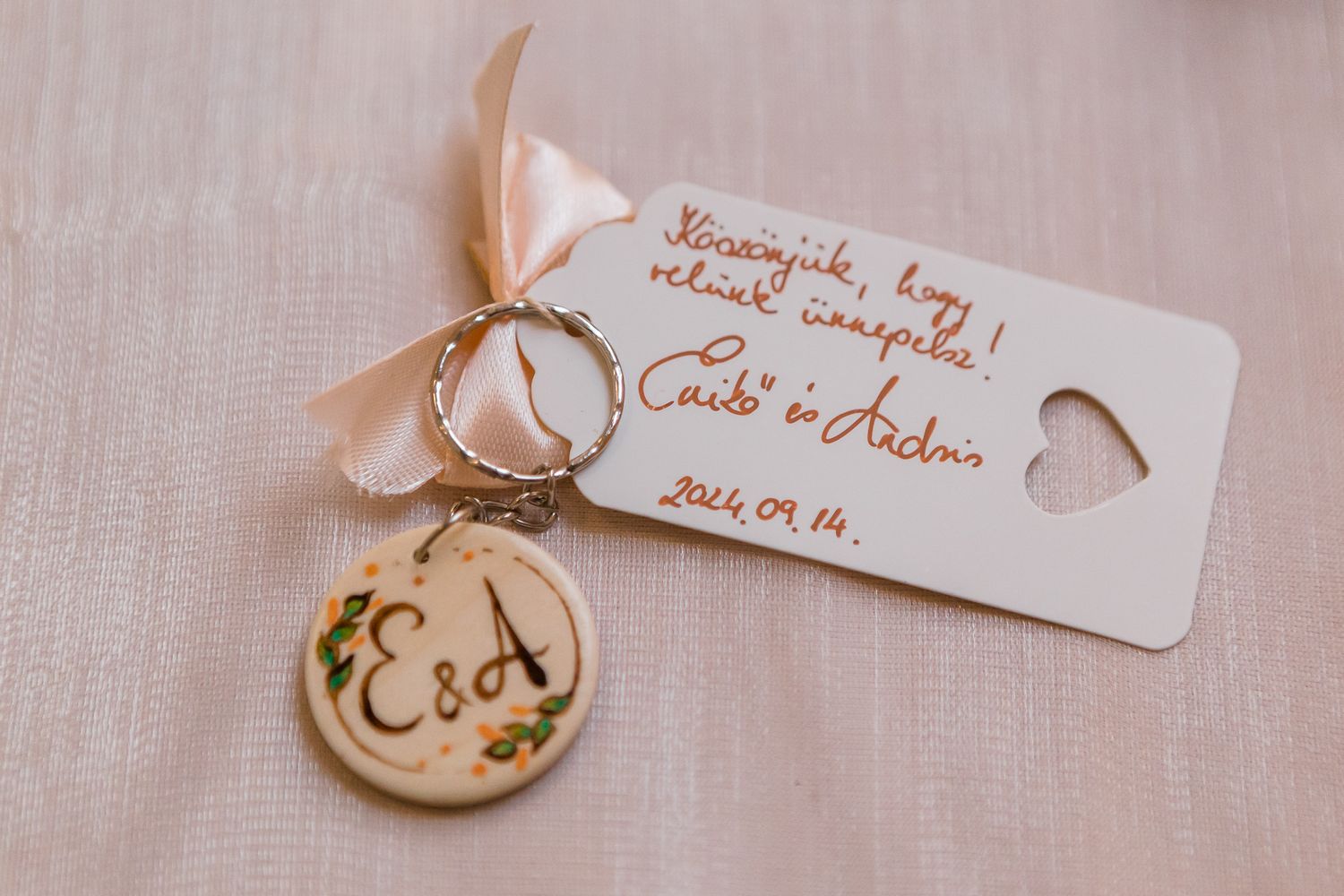 Small handwritten tags with delicate calligraphy attached to gold rings on a soft textured fabric background.