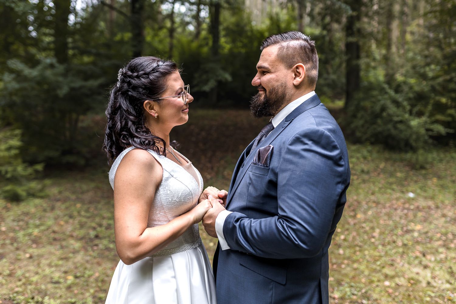 A couple in wedding attire shares intimate moments while dancing together in a wooded outdoor setting.