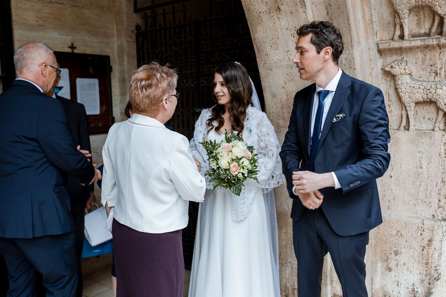 Wedding guests gather and socialize in a stone archway entrance during an elegant outdoor celebration.