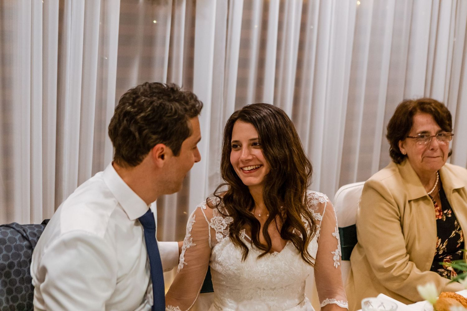 Guests seated at a wedding reception table engage in lively conversation and laughter during the celebration.