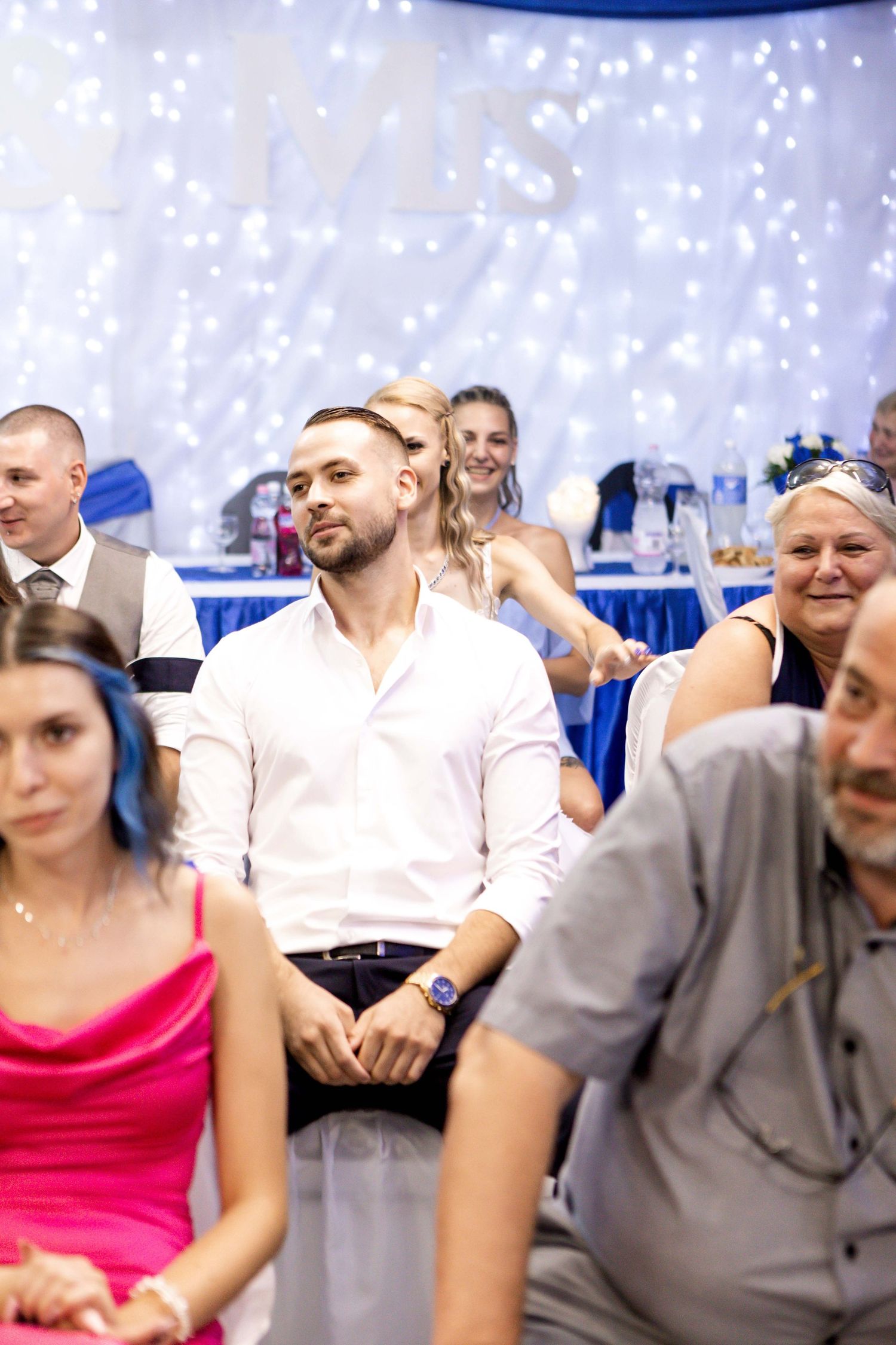 A group of guests seated at tables during a wedding reception with blue and white decor in the background.