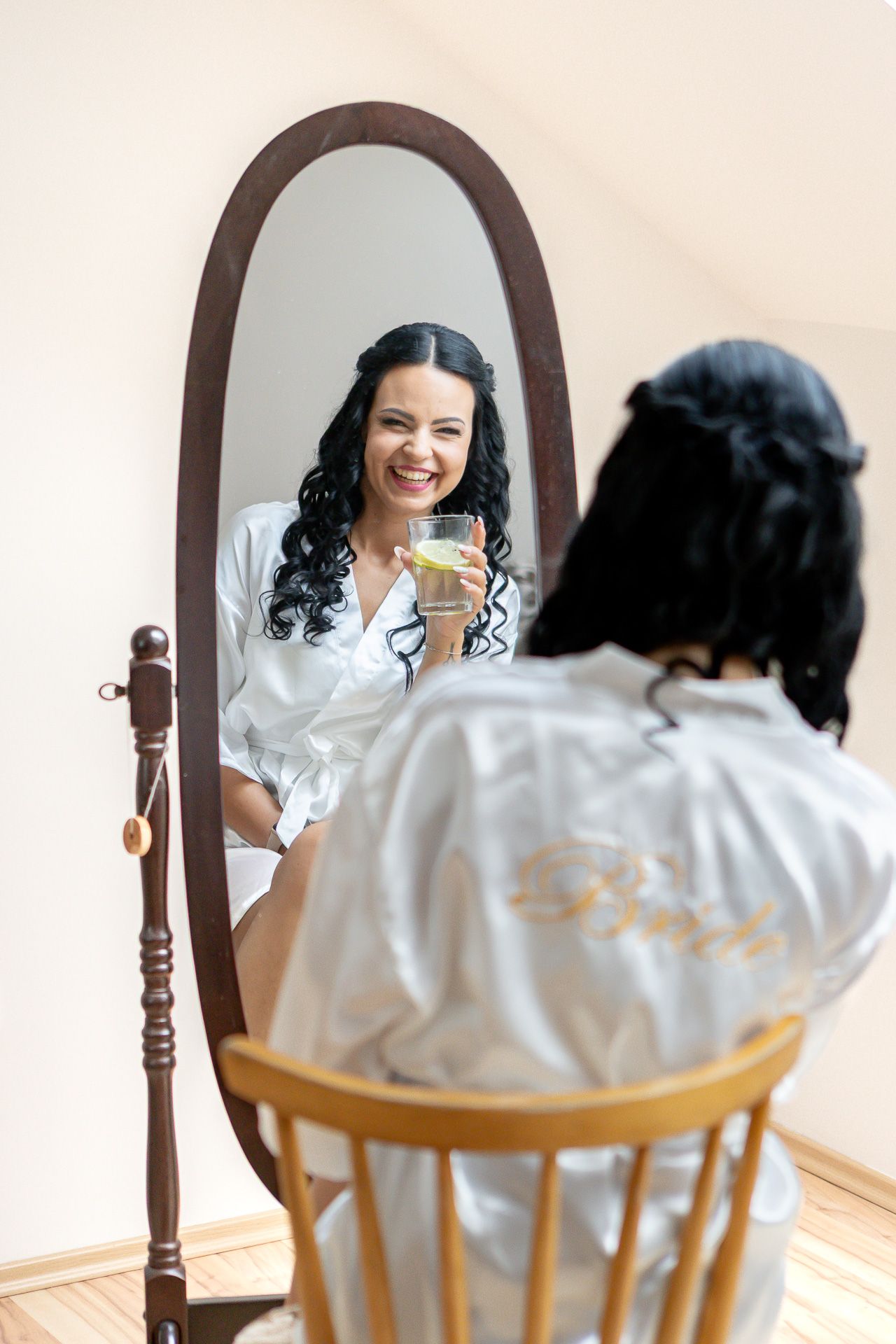 A reflection in a wooden framed mirror shows someone in a white silk robe sitting in a wooden chair.