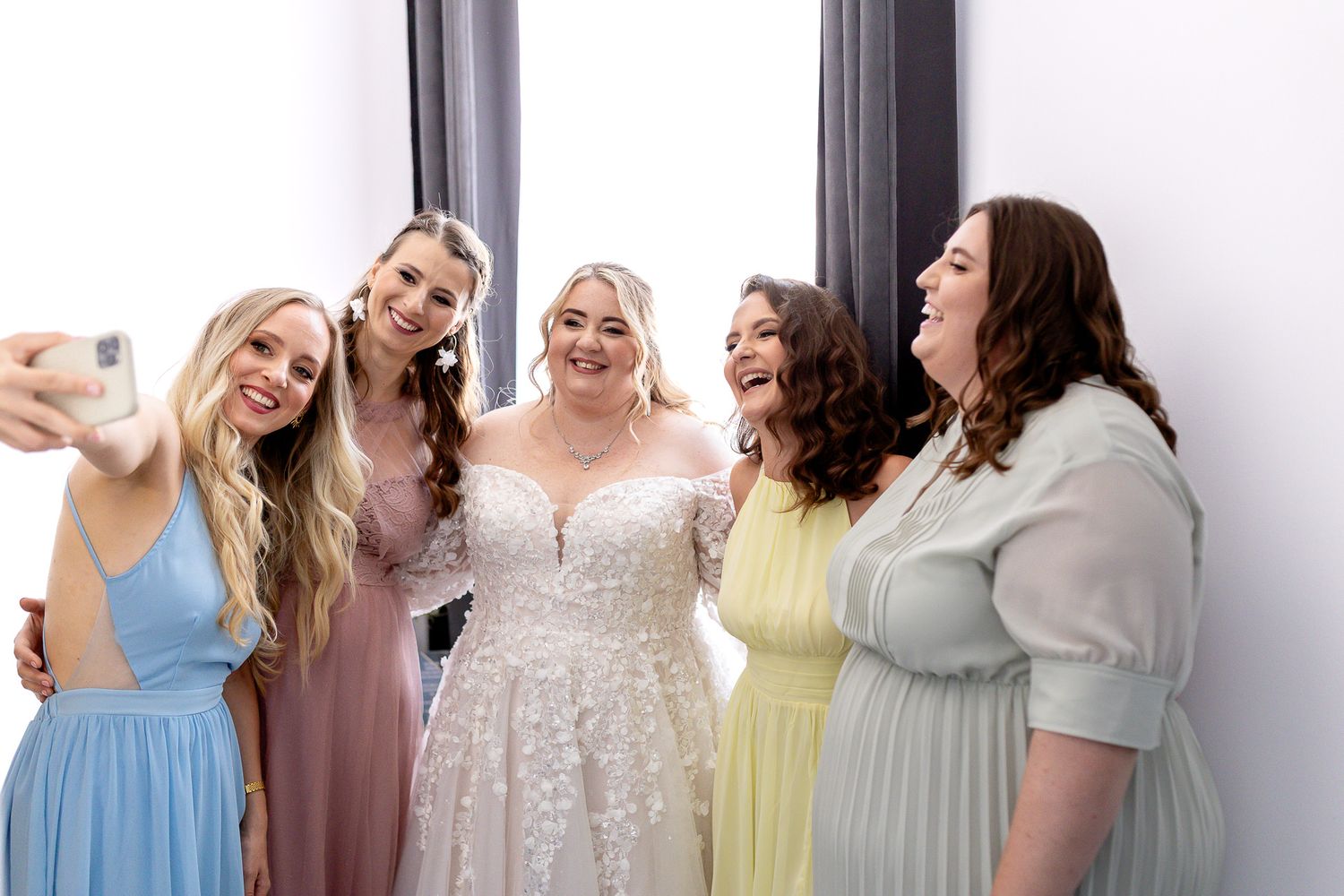 Bridesmaids in pastel dresses share joyful laughter together during a wedding photoshoot.