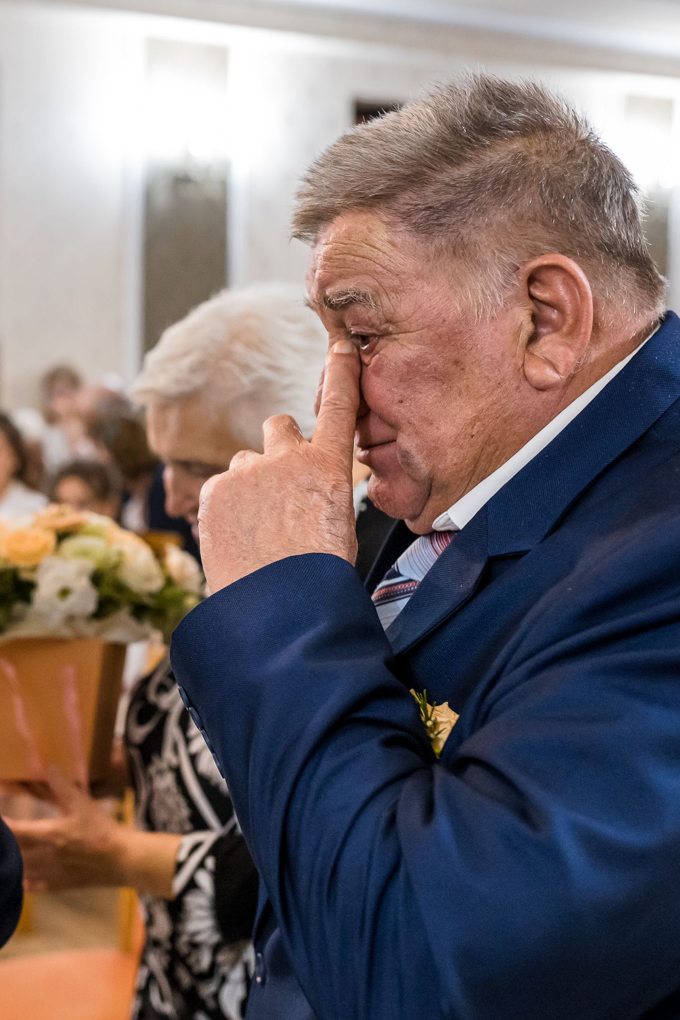 A person in a navy suit covers their face with their hand while sitting in what appears to be a courtroom setting.