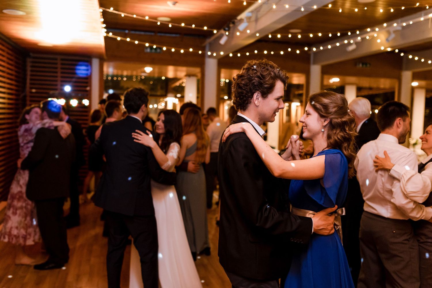 Couples dance together under warm string lights at an elegant indoor wedding reception celebration.
