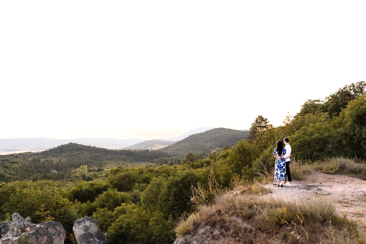 Romantic couple silhouetted against mountain landscape during sunset photoshoot.