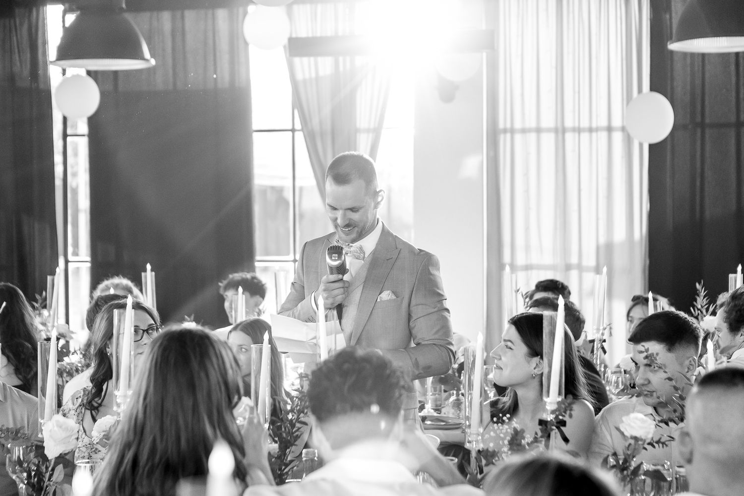 Black and white photo of wedding reception guests dancing and celebrating in an elegant venue.