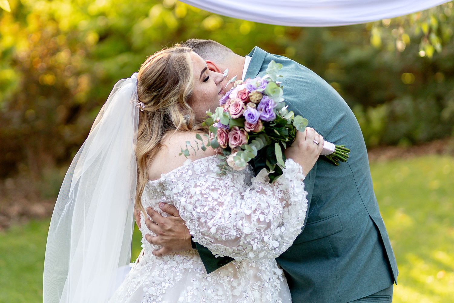 Couple embraces during outdoor wedding ceremony with white fabric draping and autumn foliage.