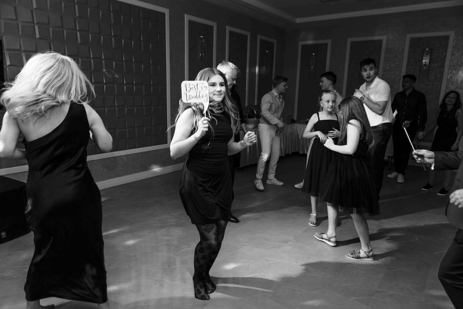 A group of dancers in black attire practicing choreography in a dimly lit dance studio.