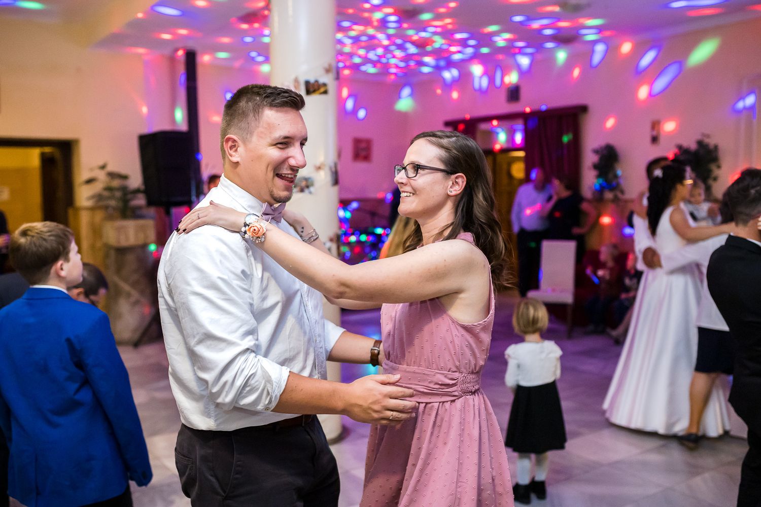 Dancers move together at a reception with colorful disco lights illuminating the venue in purple and blue hues.