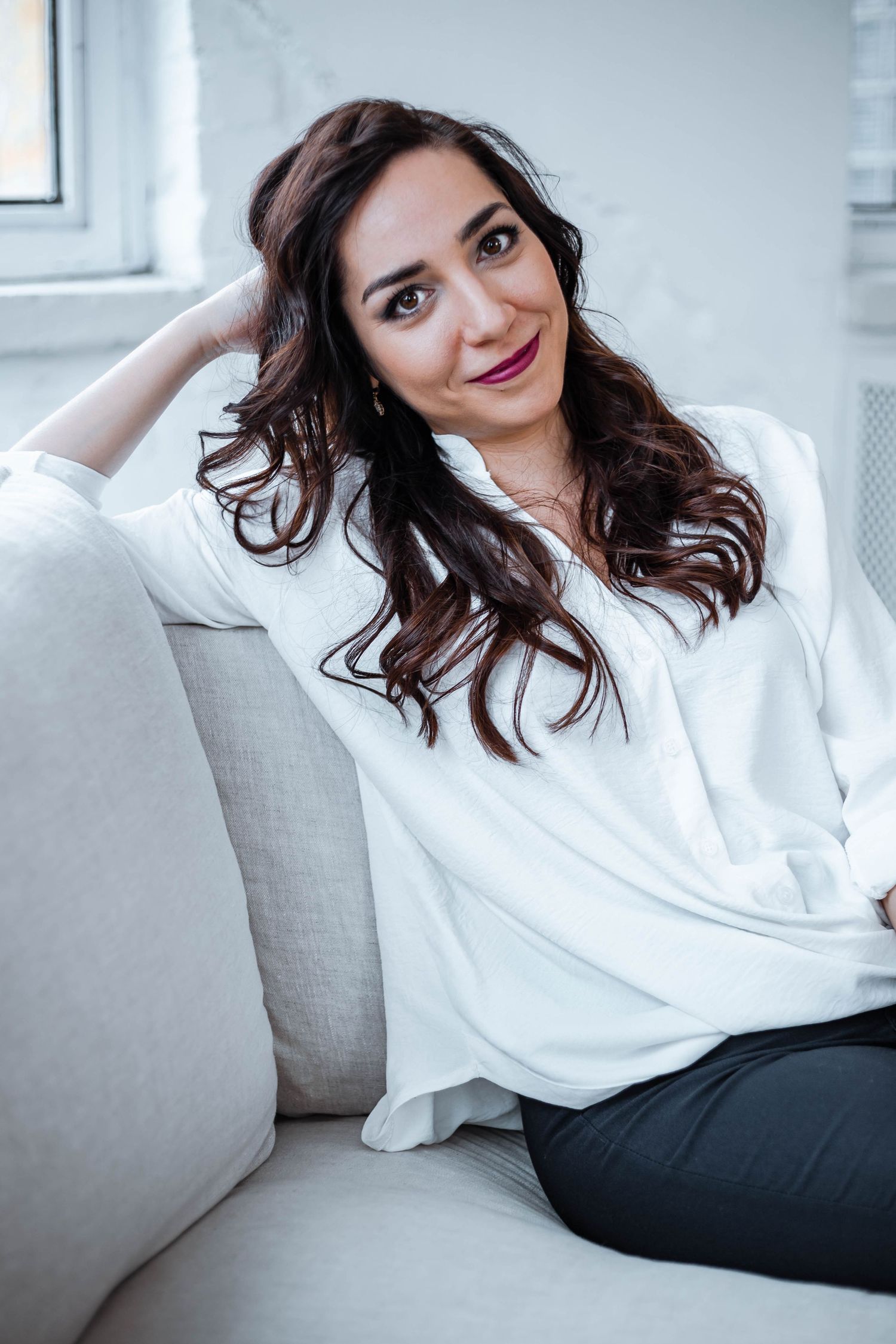 Relaxed portrait on grey couch wearing white blouse in bright modern setting.