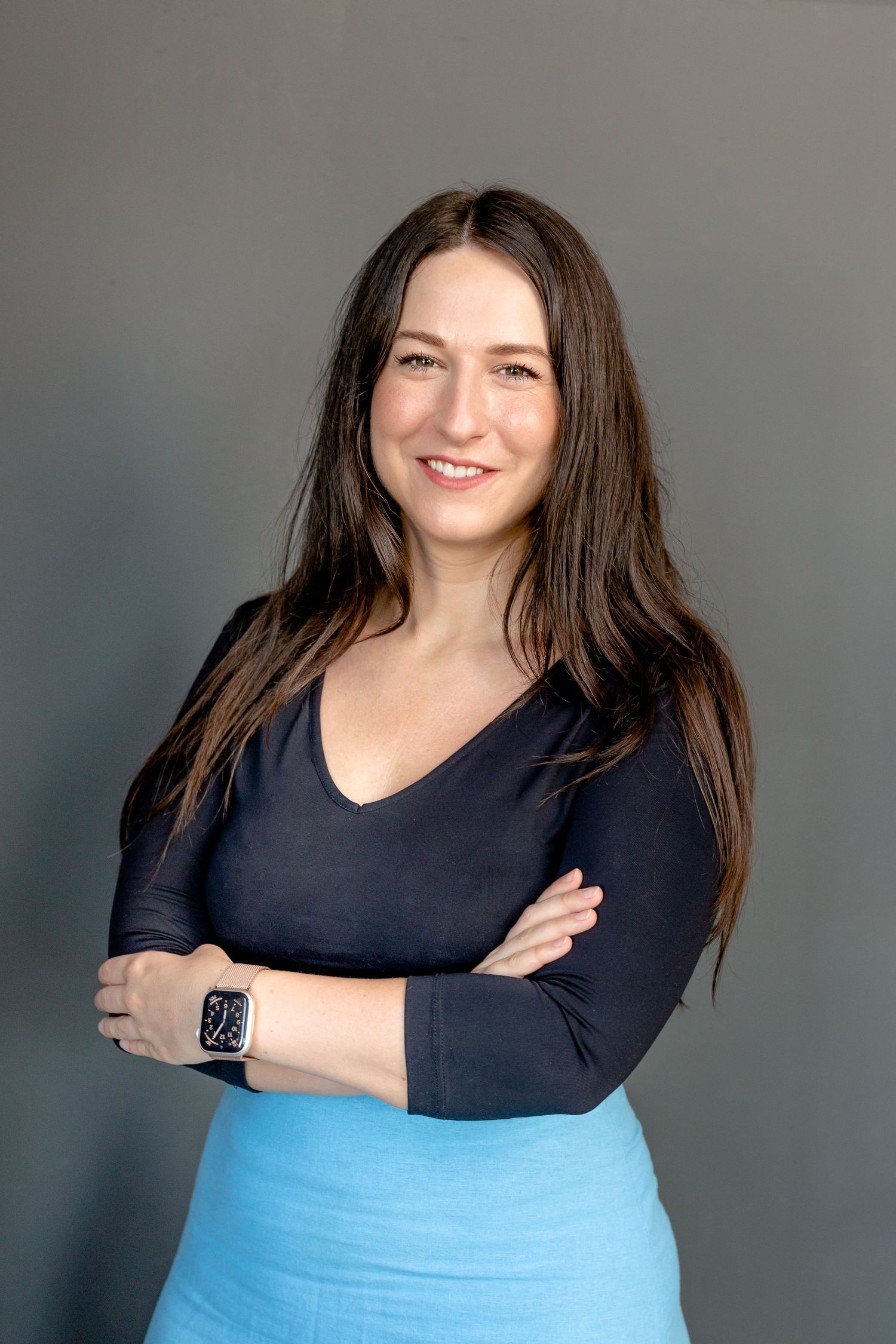 Professional portrait showing a casual business look with navy top and light blue skirt against grey background.