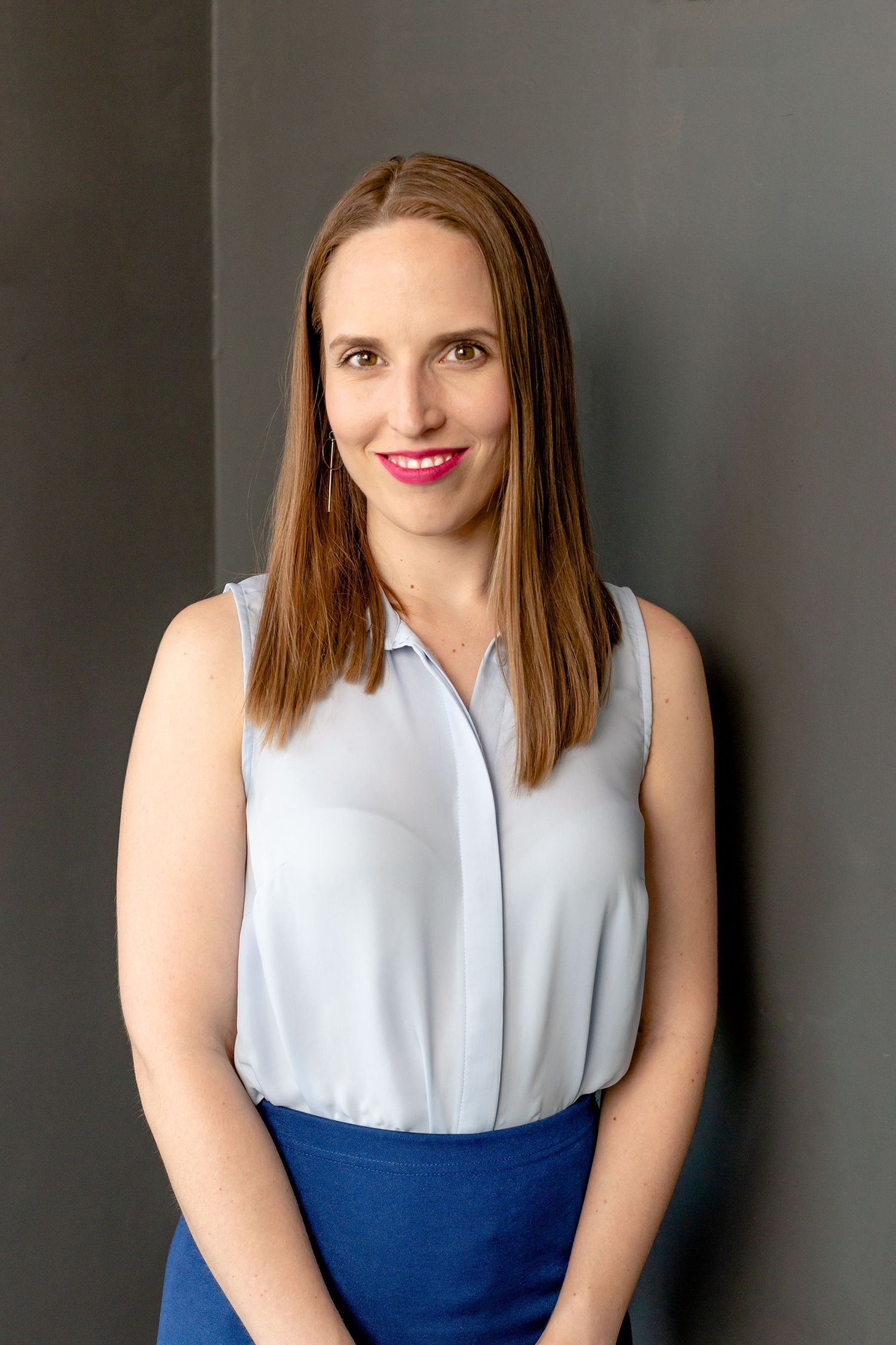 Professional portrait in a sleeveless blue and white color block dress against a dark background.