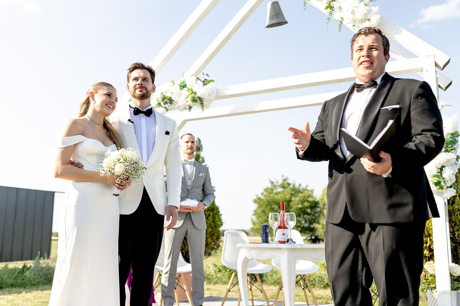 Wedding ceremony participants celebrate under white outdoor structure.