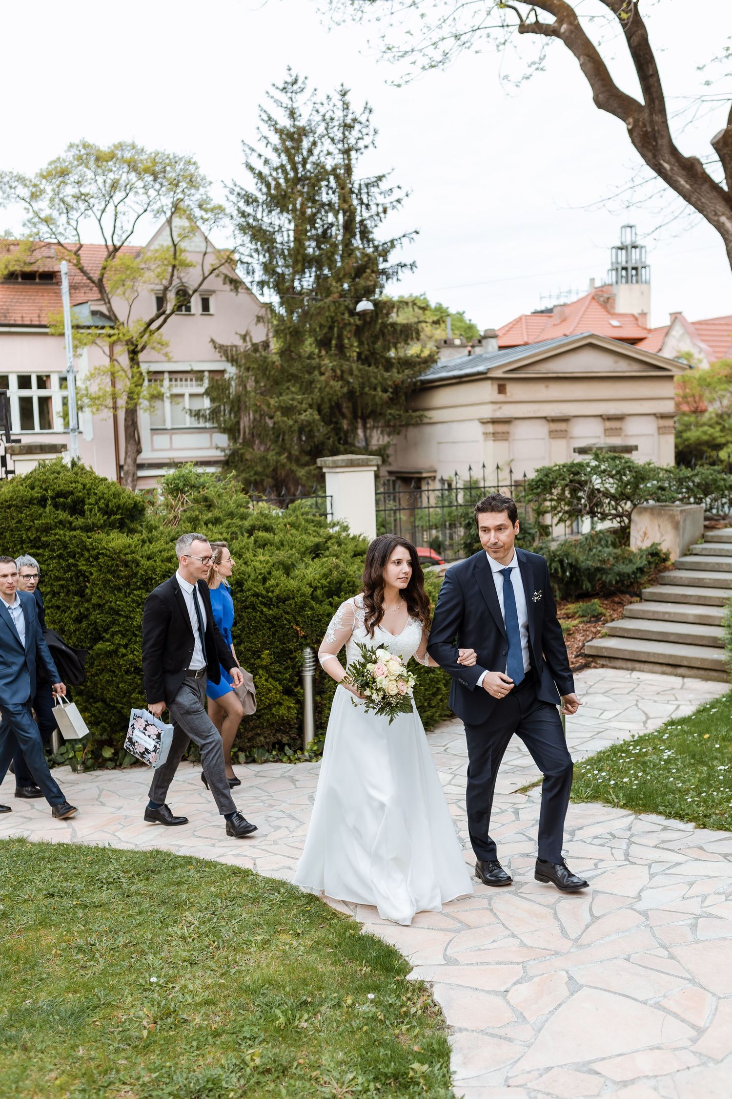 Wedding party sits on stone steps in garden during outdoor photo session.